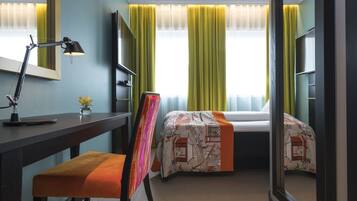 A hotel room with a desk, chair, bed, and a large mirror.