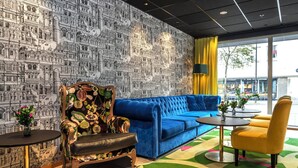 A room with a blue sofa, a floral armchair, a yellow chair, a small table, and a patterned wall.