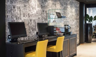 A workspace with two computer monitors, a keyboard, and a mouse on a dark desk. There are two yellow chairs and a glass display case with decorative items.