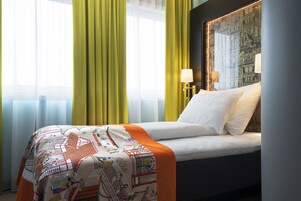 Quarto de hotel com cama, janela com cortinas, luminária e parede com padrão decorativo.