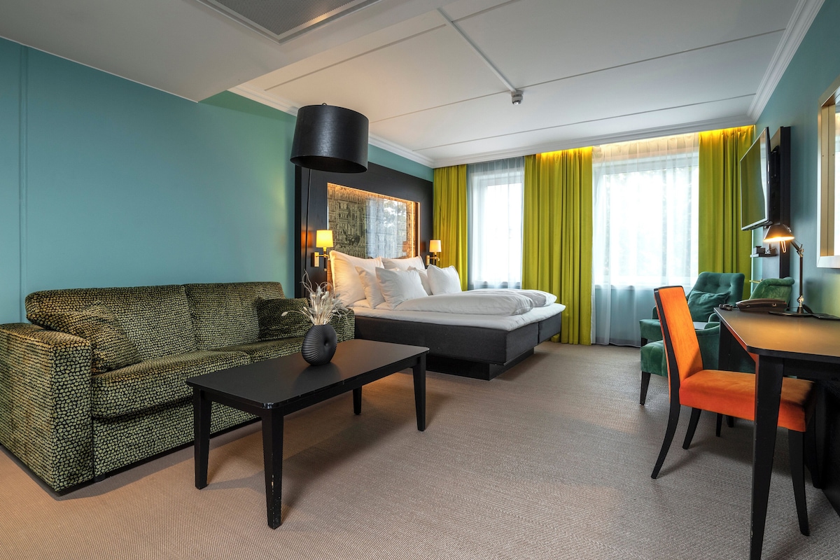 A hotel room with a bed, a sofa, a dining table, and a TV.