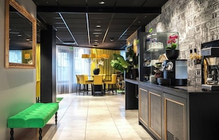 Un moderno hall de hotel con un banco verde, un área de comedor con sillas amarillas y un bar con una máquina de café.