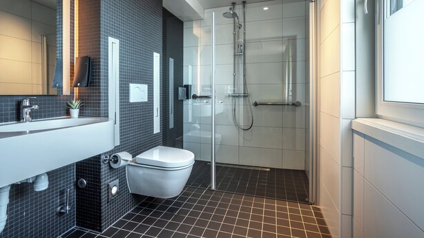 A modern bathroom with a glass shower enclosure, a white toilet, and a sink with a mirror above it. - Thon Hotel Stavanger (Stavanger)