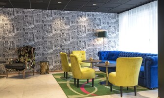 A room with a patterned wall, a blue sofa, yellow chairs, and a small round table.