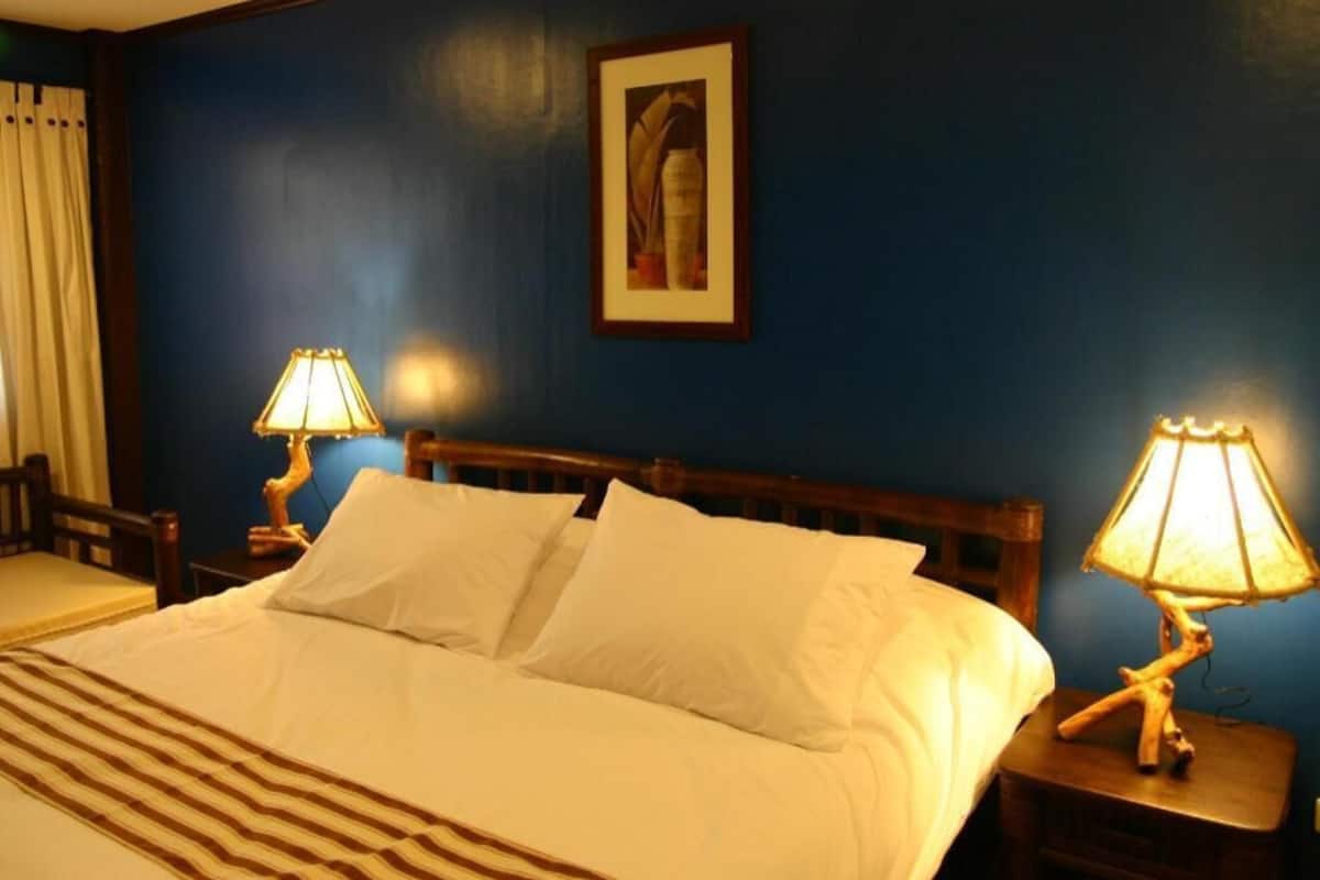 A hotel room with a bed, two bedside lamps, a framed picture on the wall, and a window with curtains.