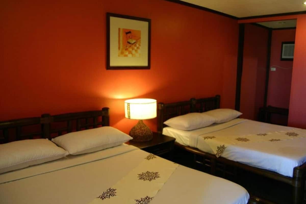 Two single beds with white linens and decorative pillows, a nightstand with a lamp, and a framed picture on the wall.