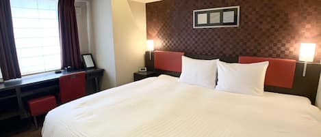 Una habitación de hotel con una cama grande, un escritorio con una silla, una ventana con cortinas y dos lámparas de noche.