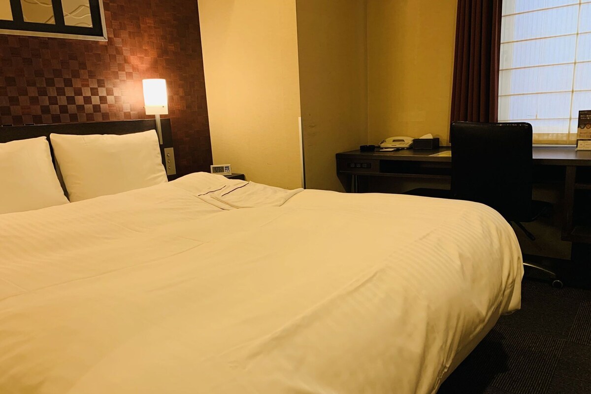 Une chambre d’hôtel avec un grand lit, un bureau avec un téléphone et une chaise.
