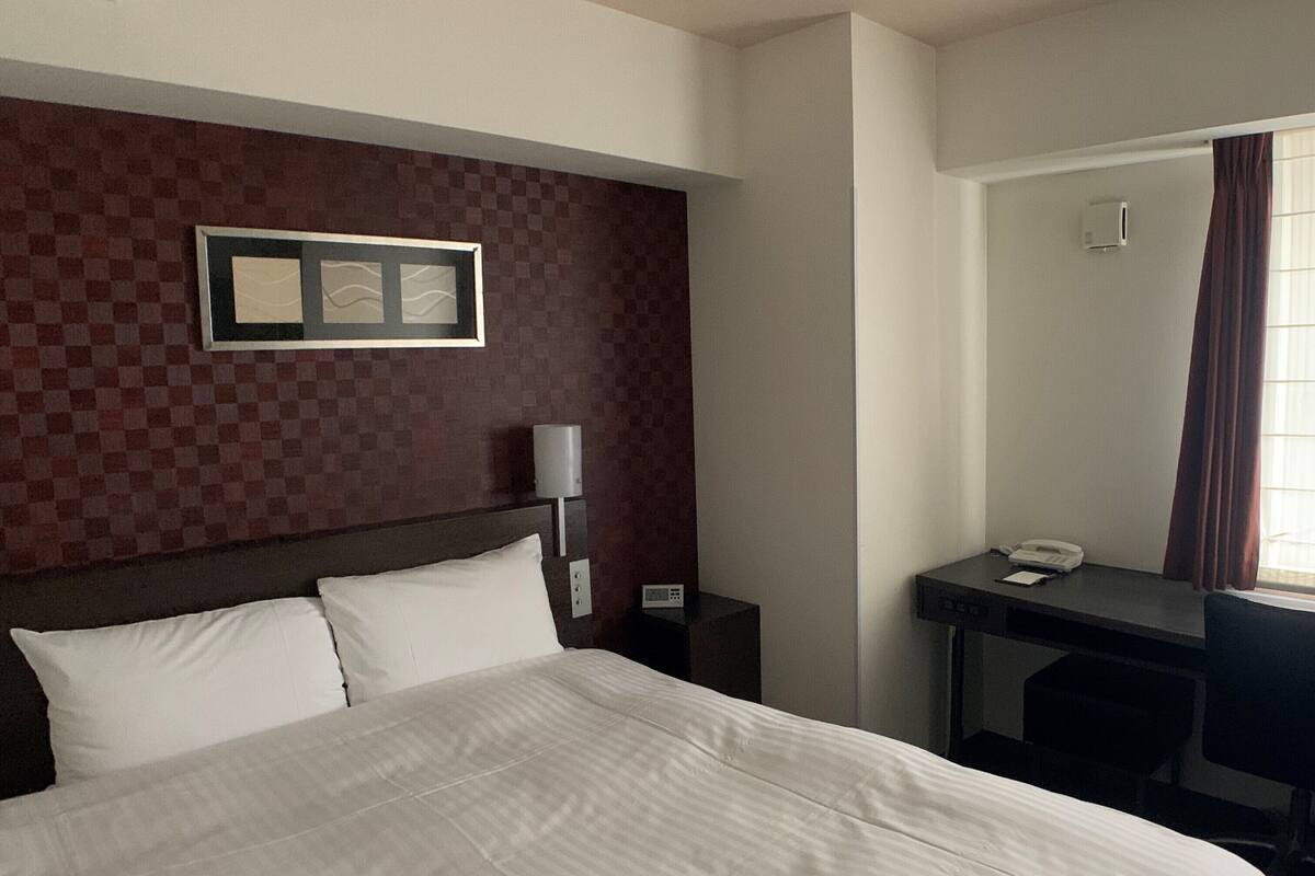 Una habitación de hotel con una cama grande, un escritorio, una silla, un teléfono y un marco de fotos en la pared.