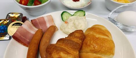 A plate with croissants, sausages, a salad, and a bowl of yogurt.