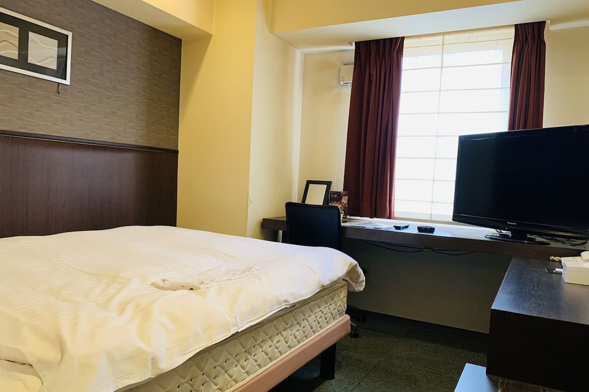 Una habitación de hotel con una cama, un escritorio con televisor y una ventana con cortinas.
