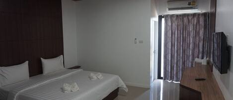 A hotel room with a large bed, a wooden headboard, a flat-screen TV mounted on the wall, and an air conditioning unit above the door.