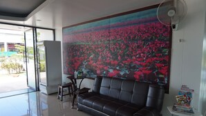 A modern interior with a black leather sofa, a glass table, and a large floral mural on the wall. - NN Place (Udon Thani)