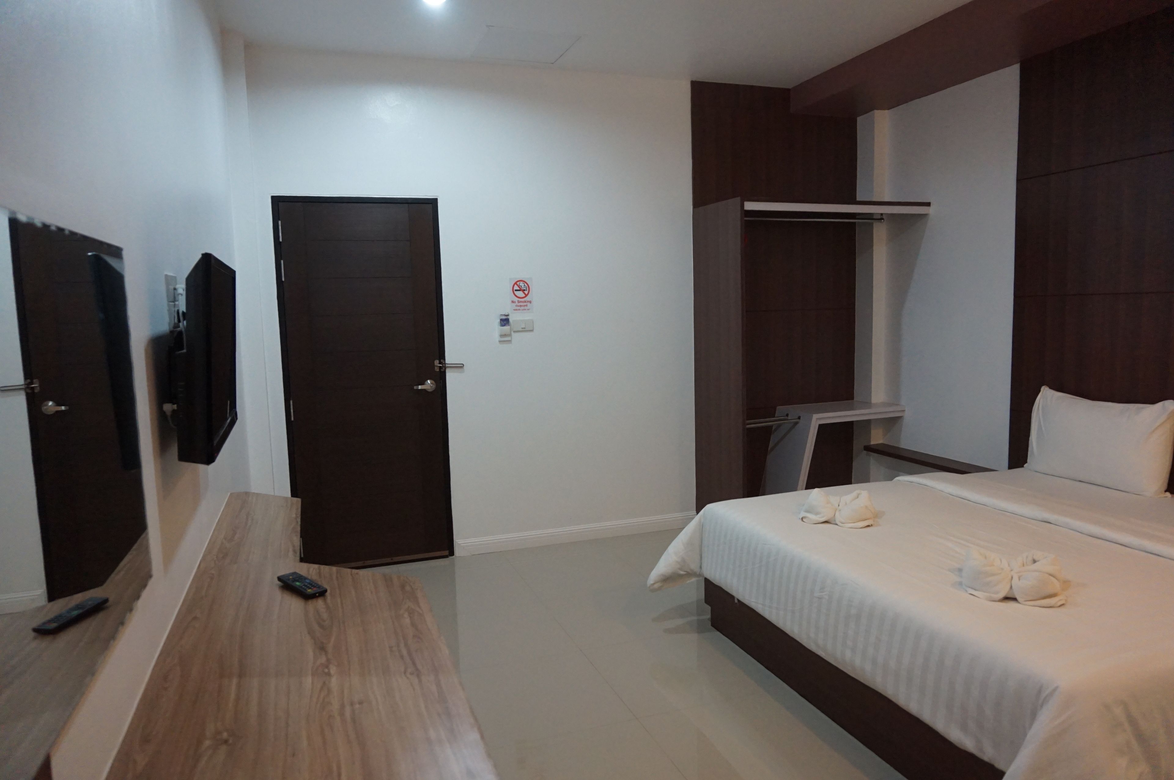 Ein Hotelzimmer mit einem Bett, einem Holztisch, einem an der Wand befestigten Fernseher und einem Kleiderschrank.