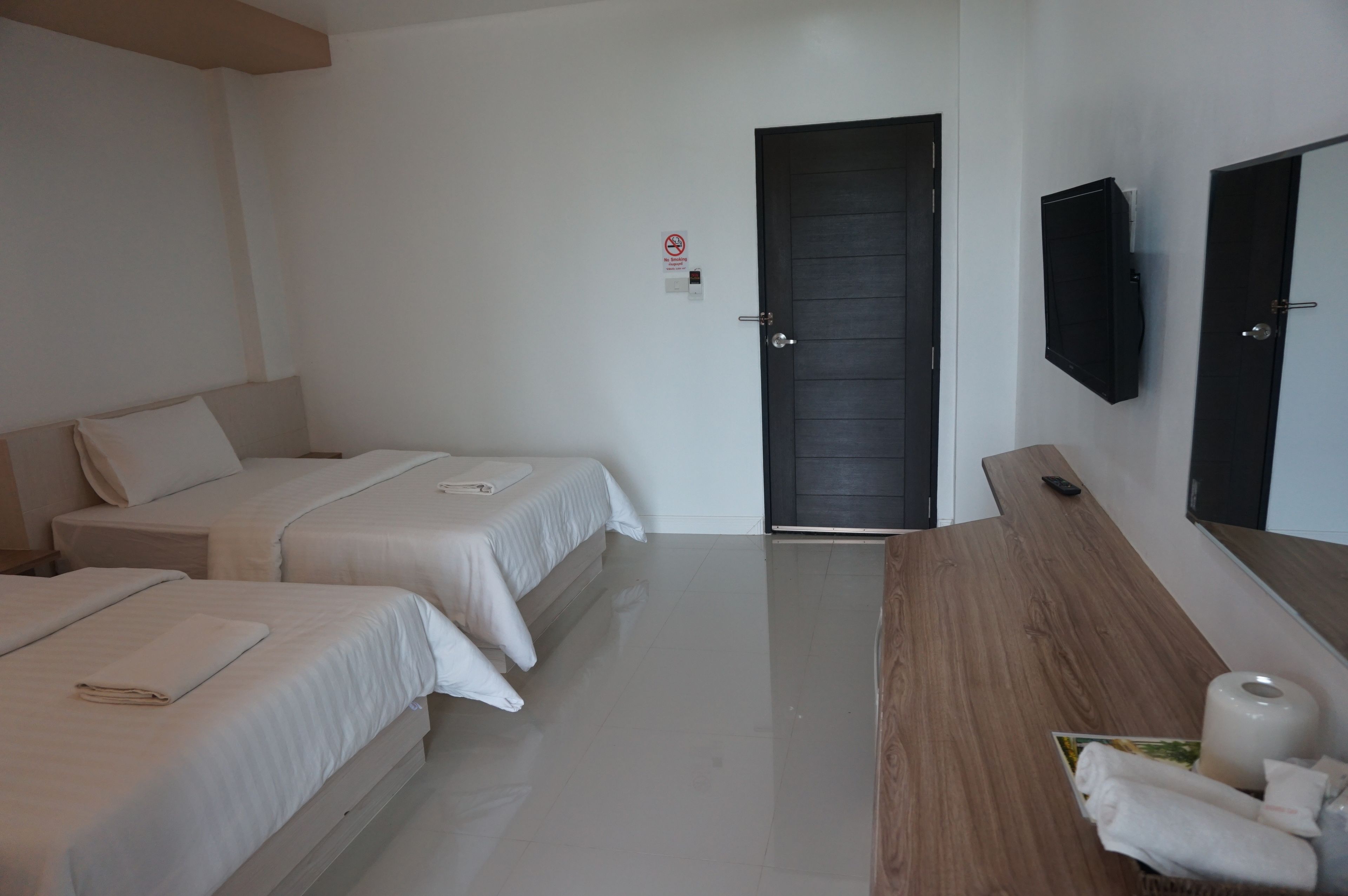 A hotel room with two beds, a wooden desk, a TV mounted on the wall, and a door with a sign.