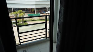 A balcony with a view of a commercial area, including a building with a white roof and parked cars. - NN Place (Udon Thani)