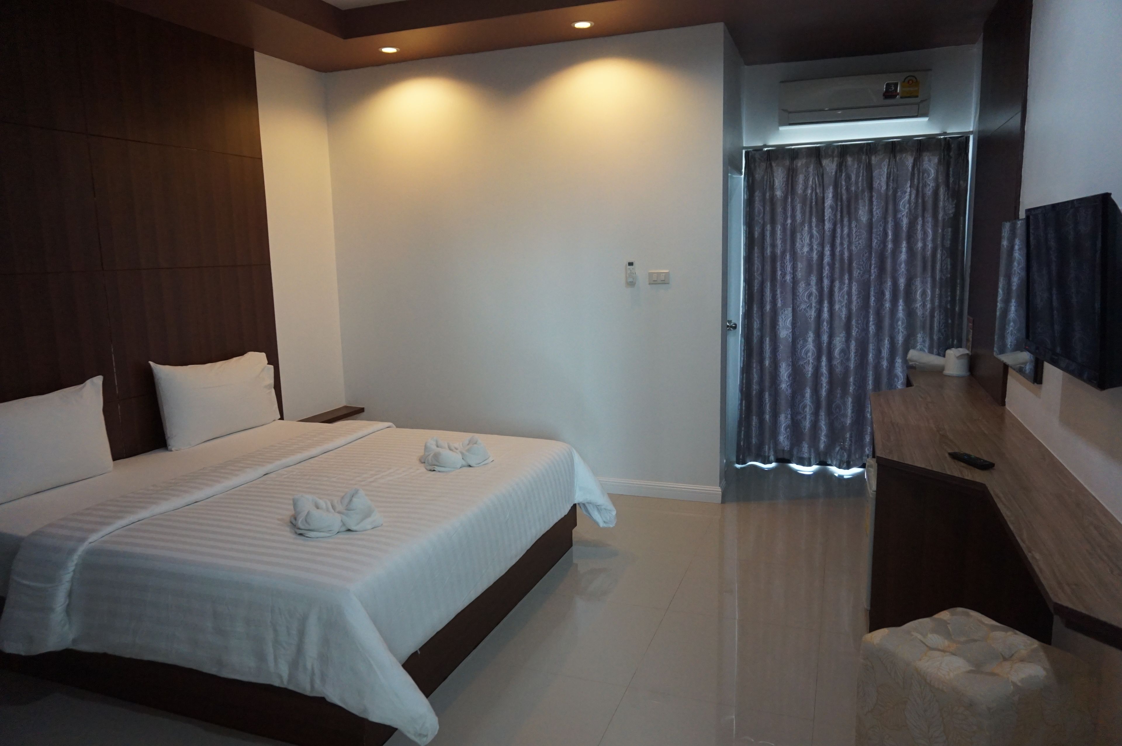 Une chambre d’hôtel avec un grand lit, une tête de lit en bois, un téléviseur à écran plat, un petit coin salon et une fenêtre avec des rideaux.