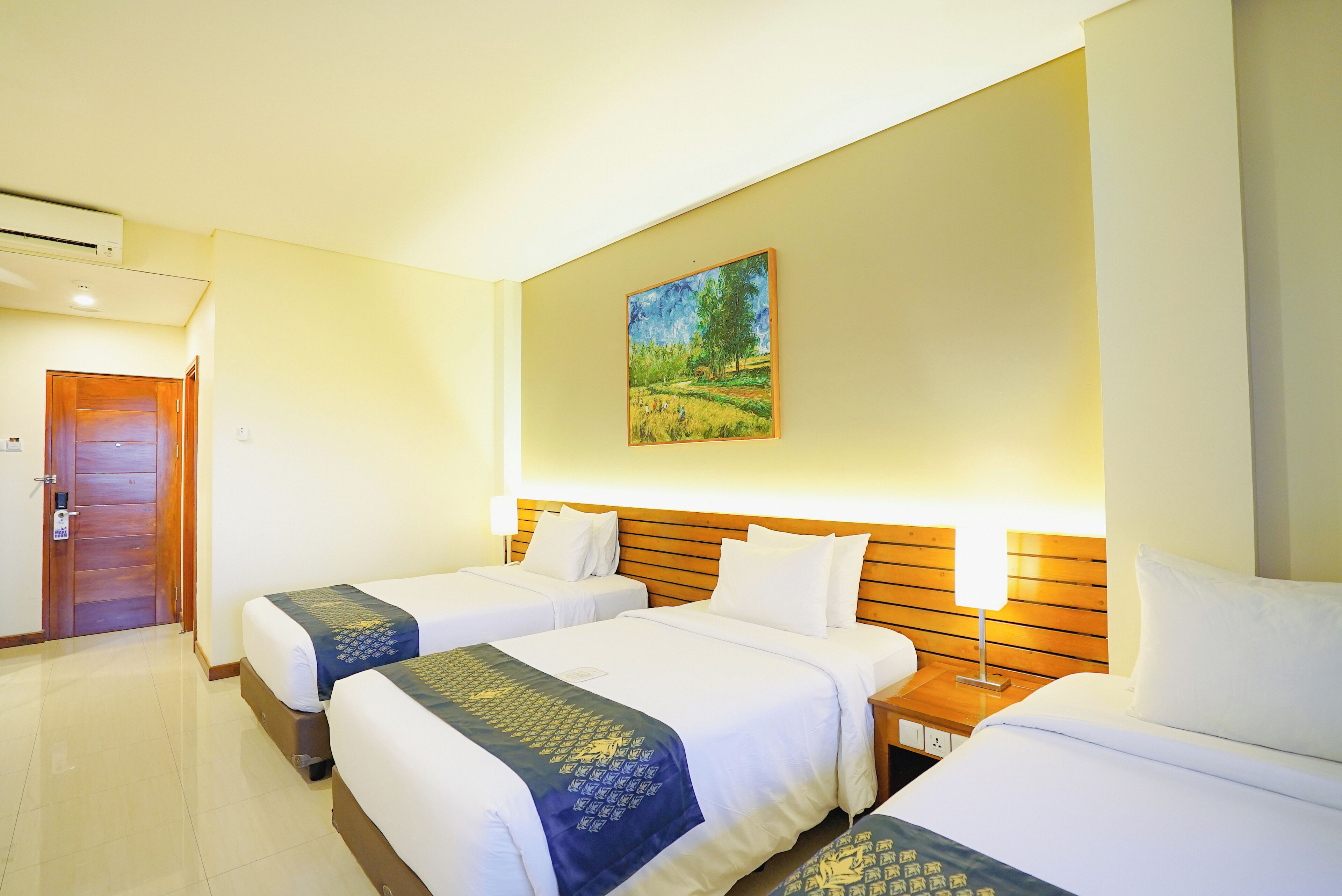 A hotel room with two beds, a wooden headboard, a painting on the wall, and a door.