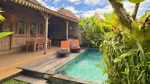 A poolside area with a wooden deck, lounge chairs, and a covered seating area with a tiled roof. - Royal Casa Ganesha (Mas)