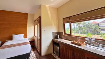 Habitación de hotel con cama, una kitchenette pequeña y ventana que ofrece vista a palmeras y un edificio.