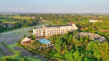 Un hotel de varios pisos, rodeado de exuberante vegetación y campos de arroz.