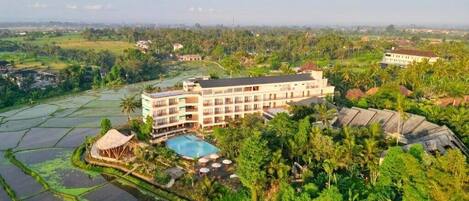 Un hotel de varios pisos, rodeado de exuberante vegetación y campos de arroz.