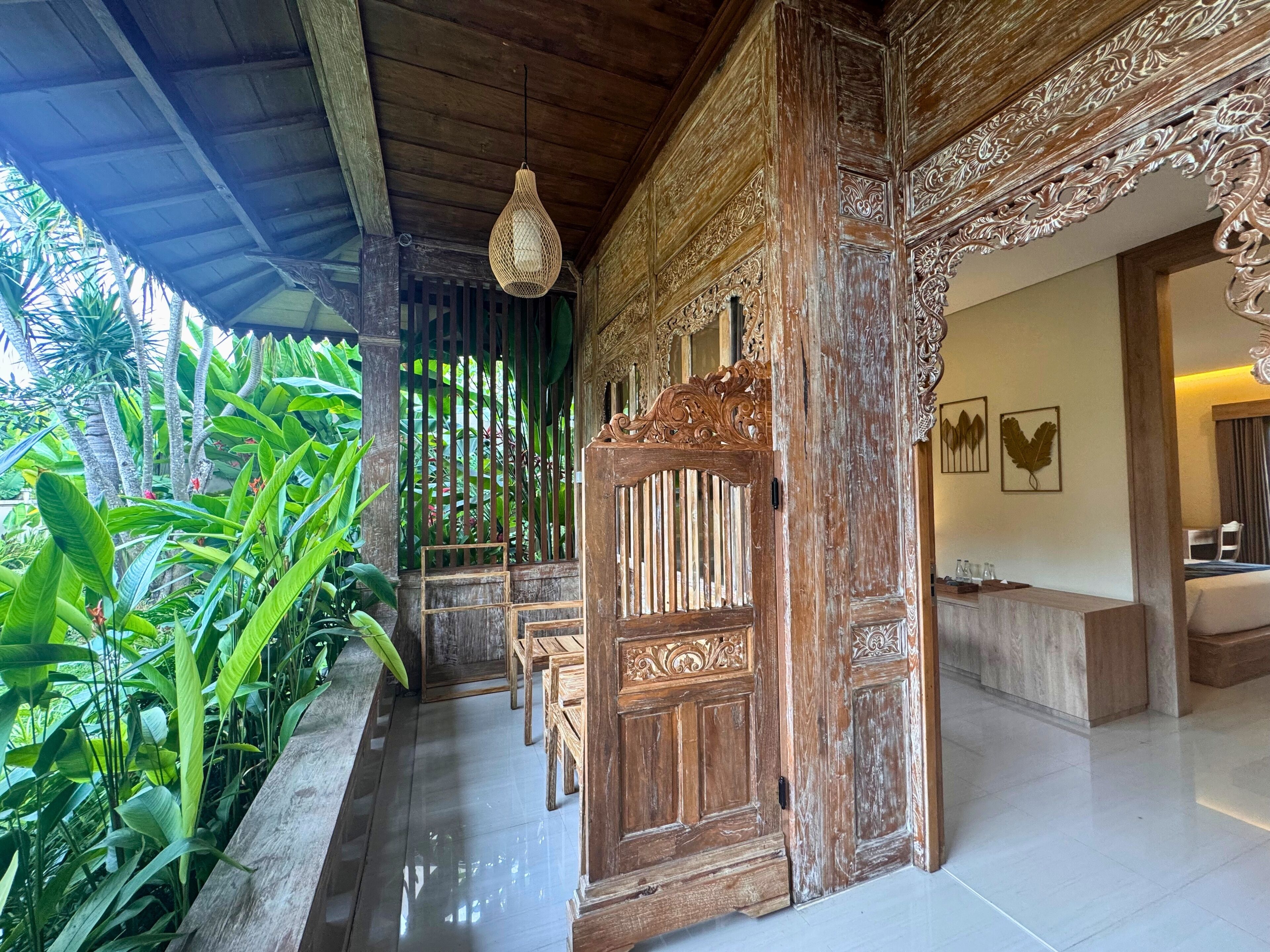 A traditional wooden door with intricate carvings, a hanging light fixture, and a view of a lush green garden.