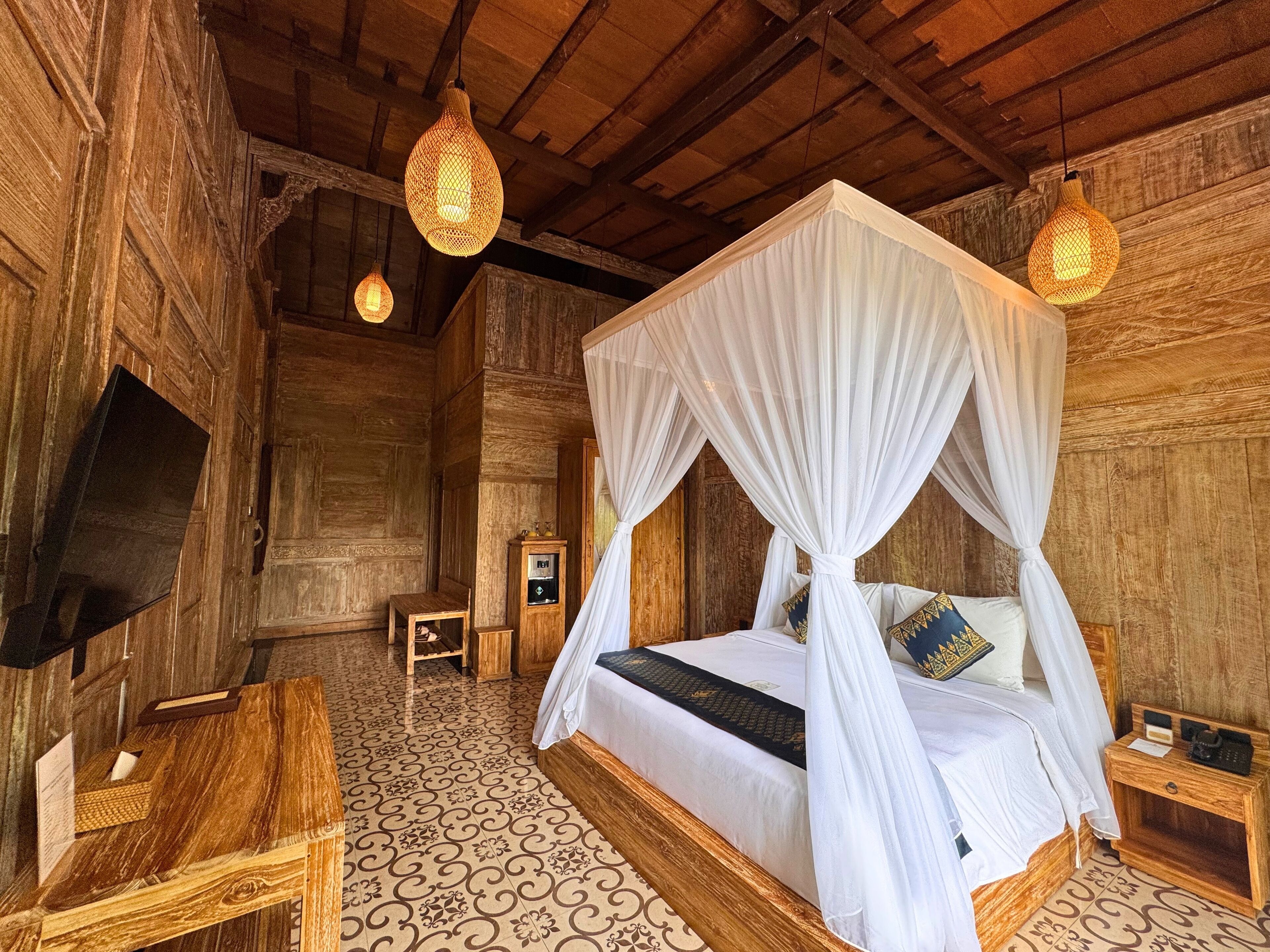 A wooden room with a four-poster bed, a television, and a small table with a lamp.