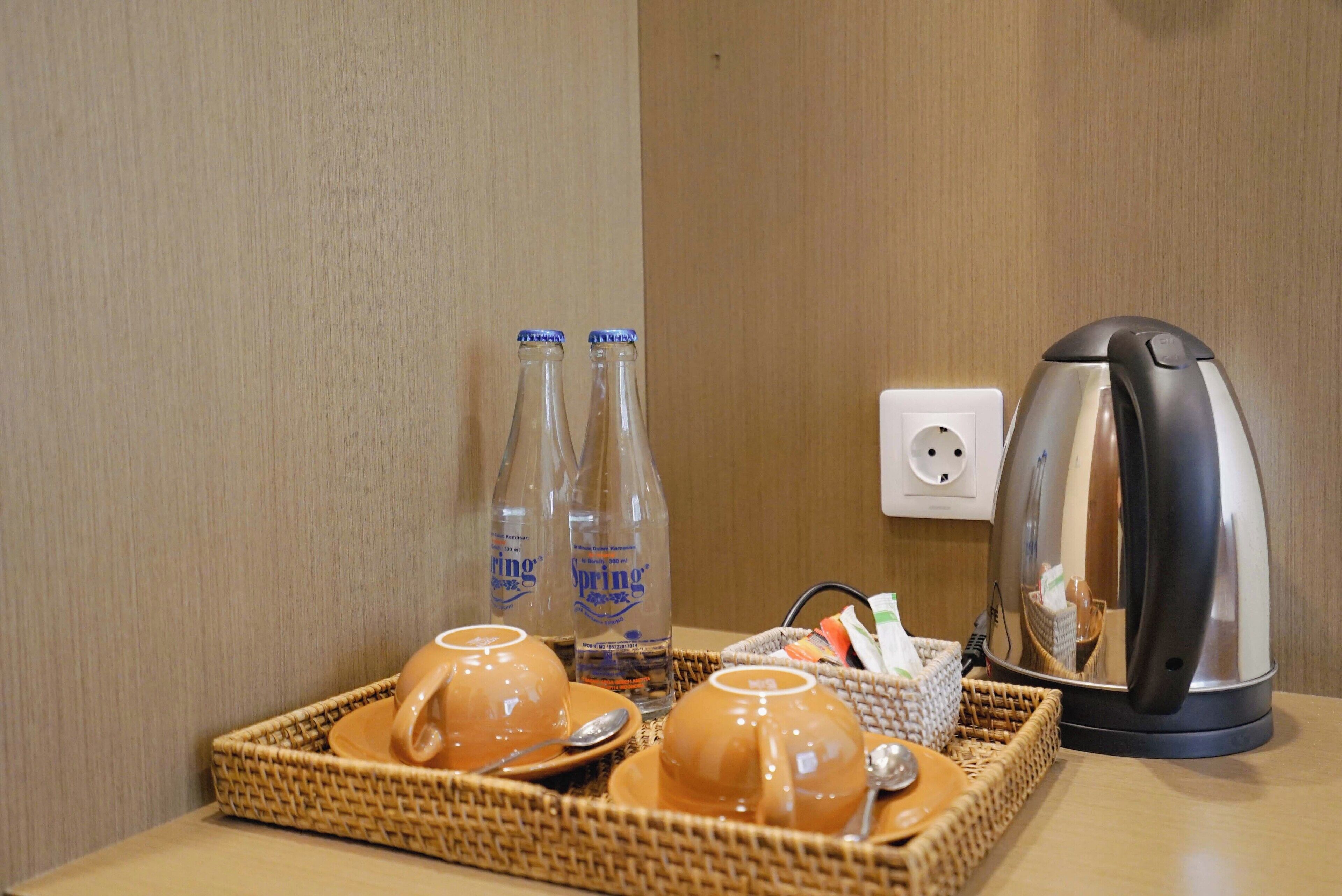A tray with two cups, two bottles of water, a kettle, and a basket with utensils on a wooden table.