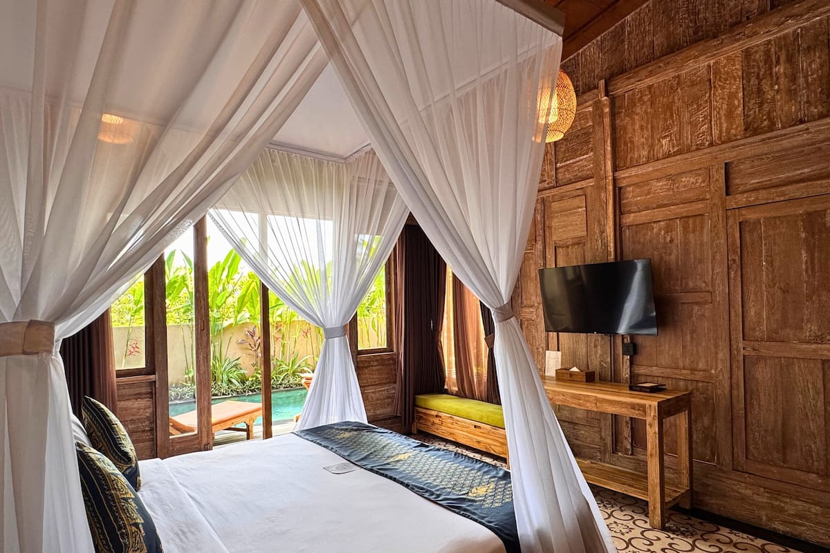 A bedroom with a bed, a TV, and a view of a pool.
