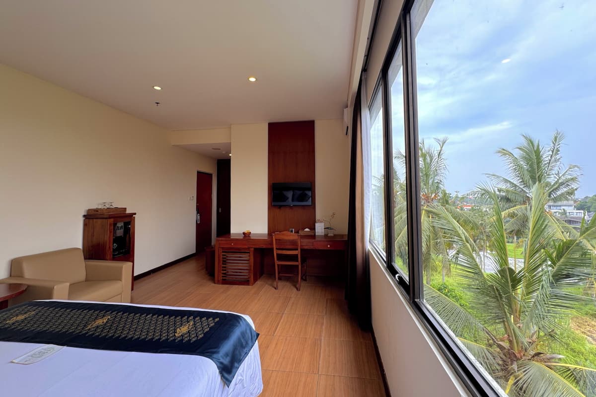 A hotel room with a bed, a desk, a chair, and a view of palm trees.