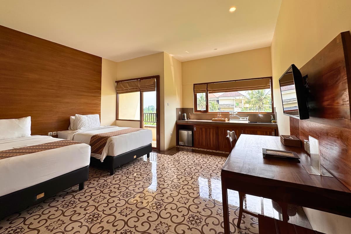 A hotel room with two beds, a dining table, a kitchen area, and a large window with a view of greenery.