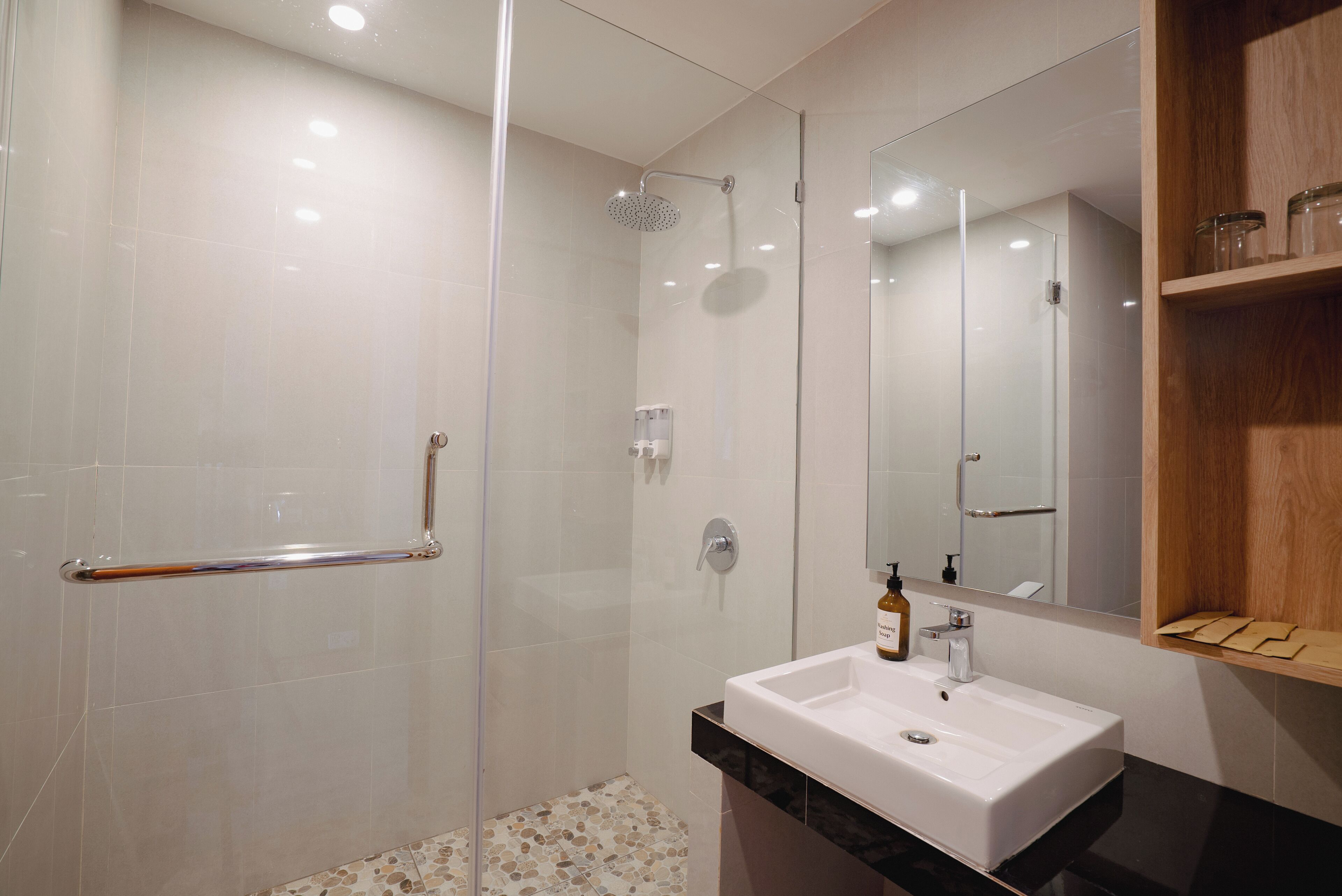 A modern bathroom with a glass shower enclosure, a white sink, and a wooden shelf with jars.