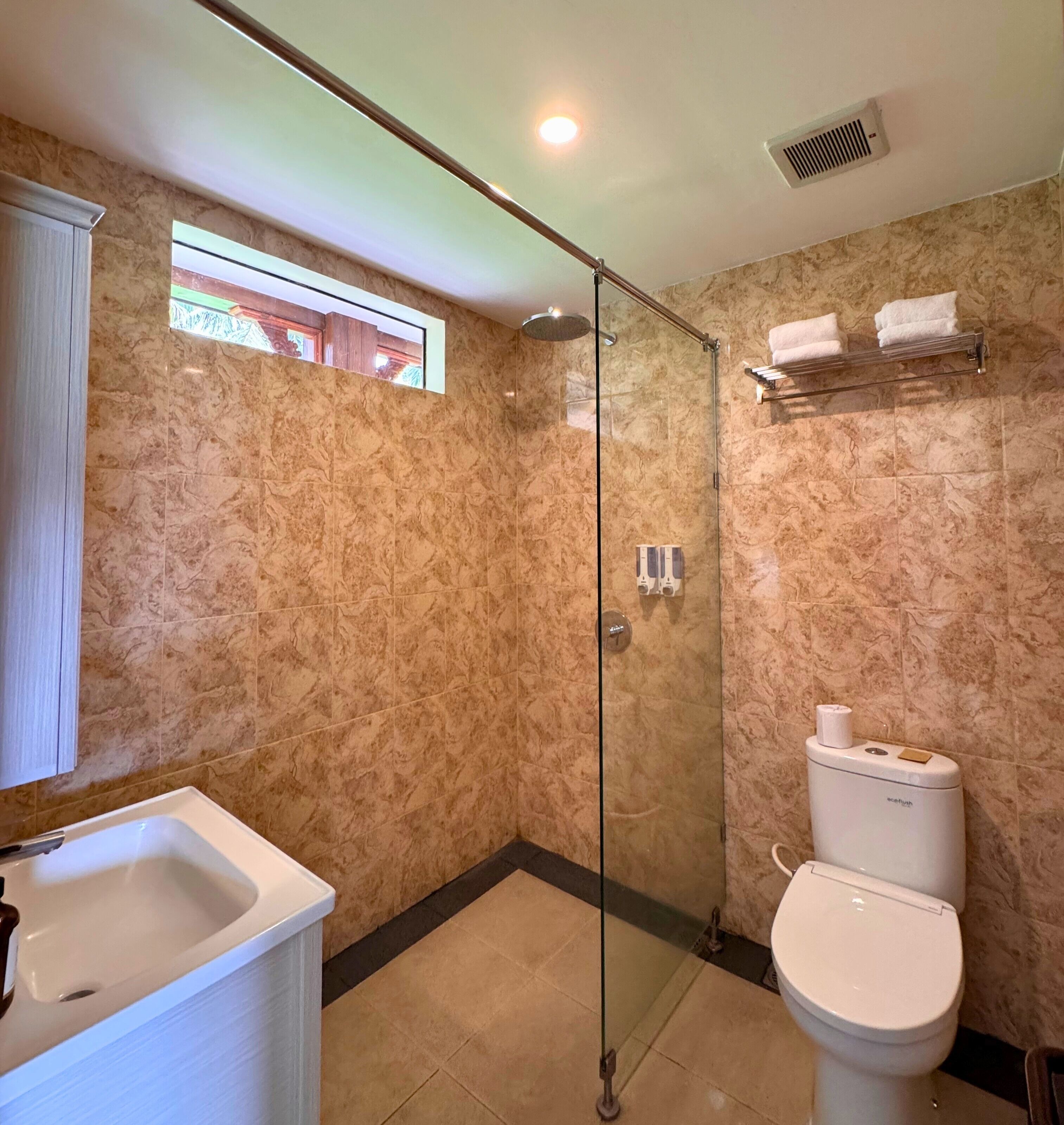 Un baño con cabina de ducha de vidrio, inodoro y lavamanos.