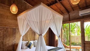 A four-poster canopy bed with a wooden headboard, white bedding, and decorative pillows. - Royal Casa Ganesha (Mas)