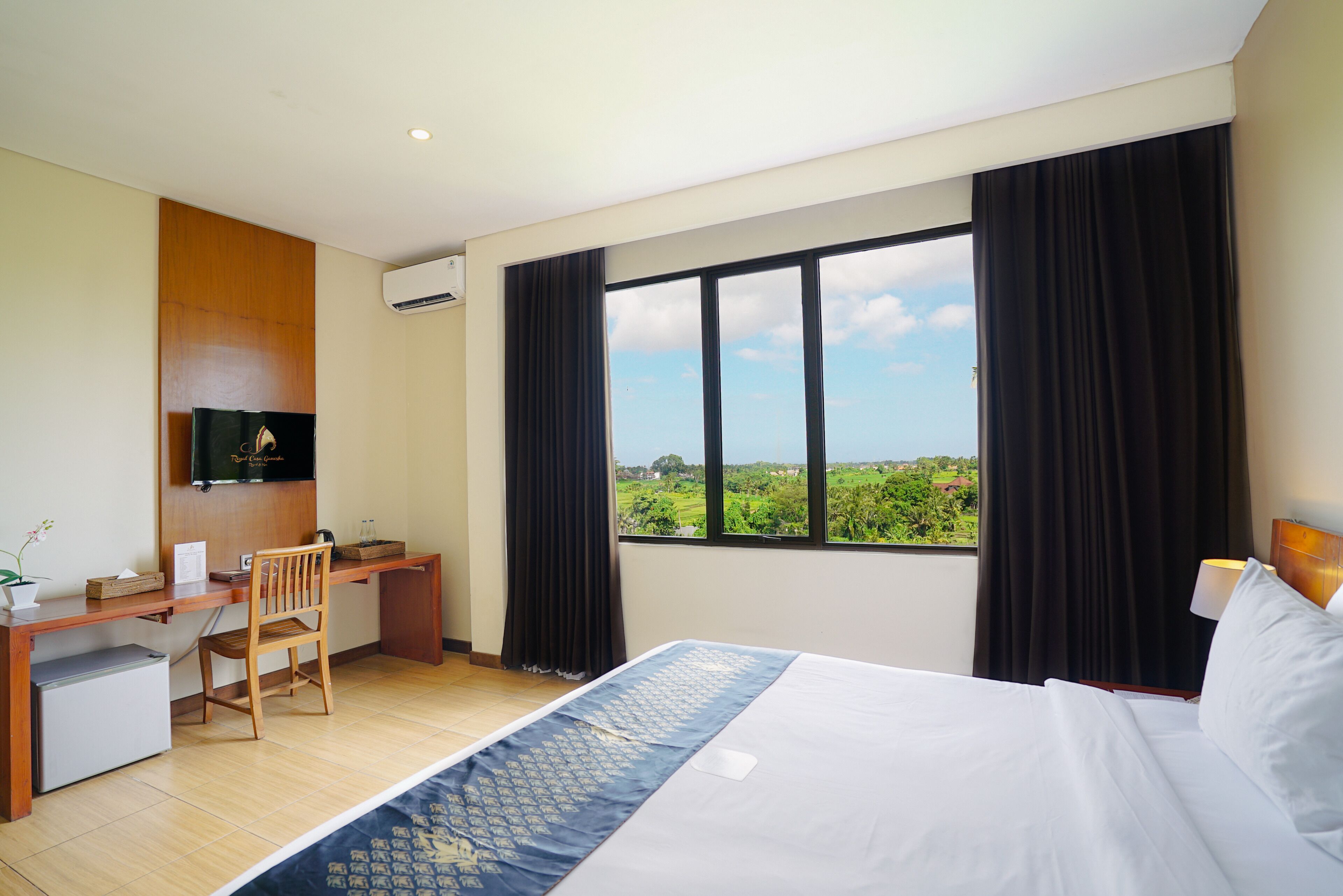 Quarto de hotel com cama, escrivaninha, cadeira, televisão e uma janela grande com vista.