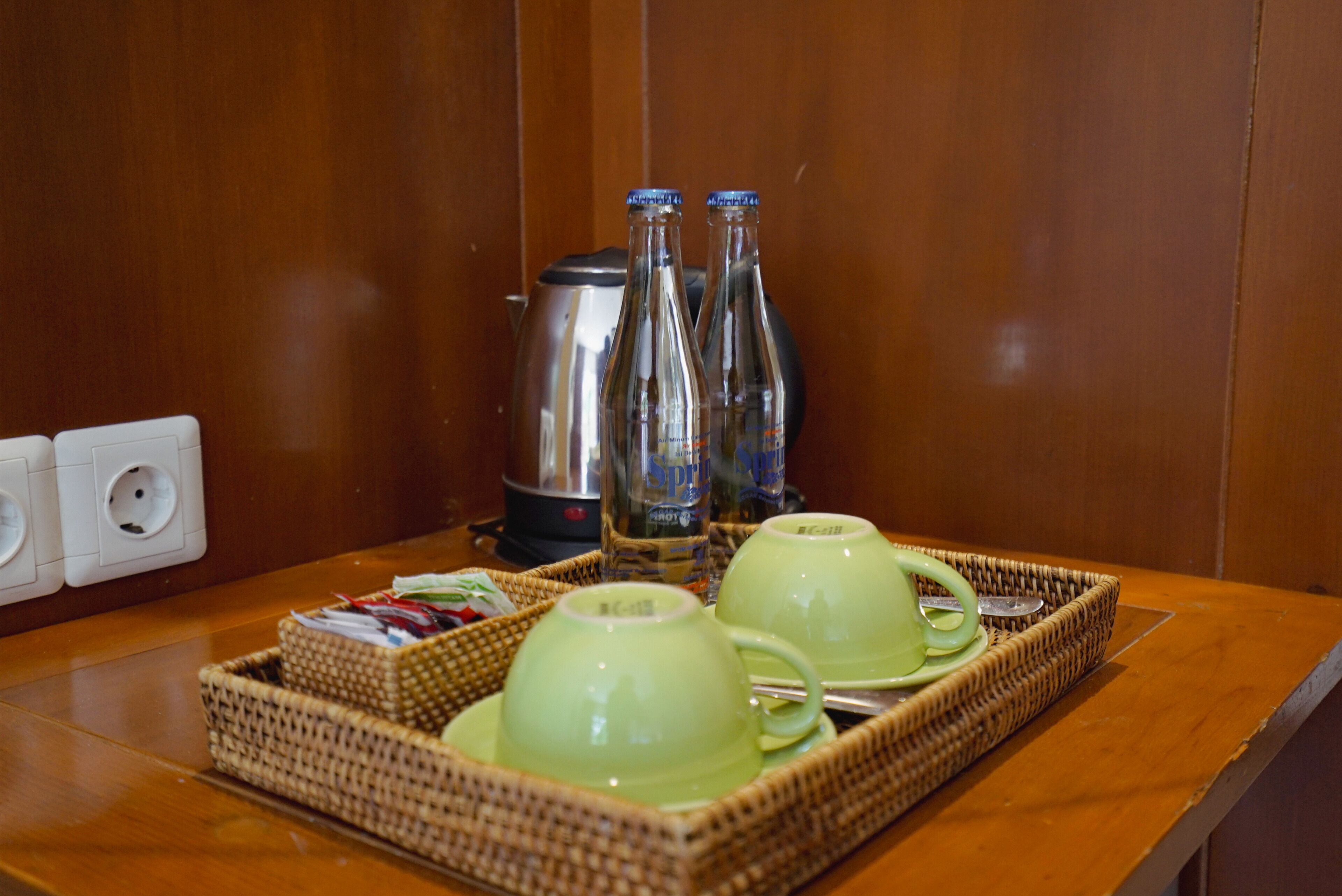 A tray with two green cups and two bottles on a wooden table.