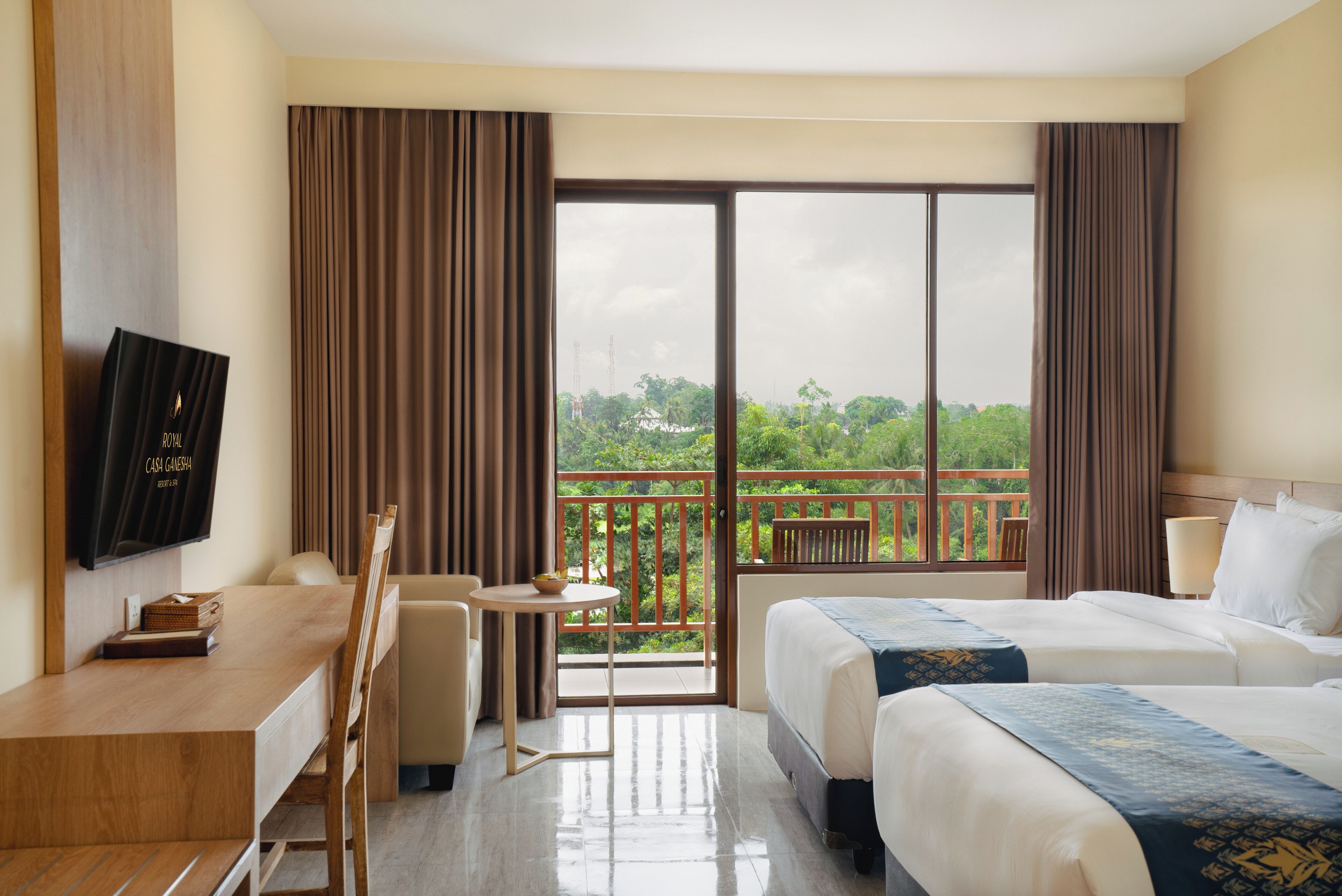 A hotel room with a balcony, a desk with a chair, two beds, and a television on the wall.