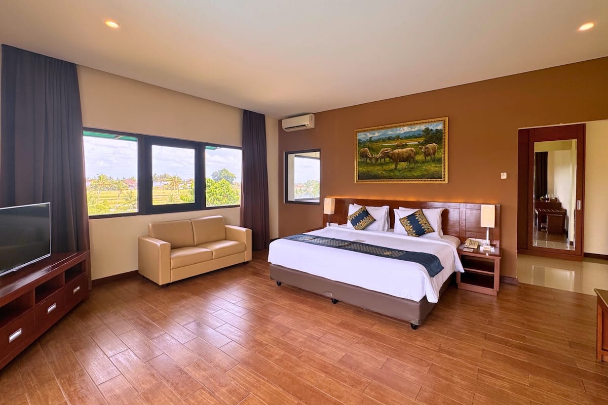 A hotel room with a bed, a TV, a sofa, a painting, and a view of the outdoors.