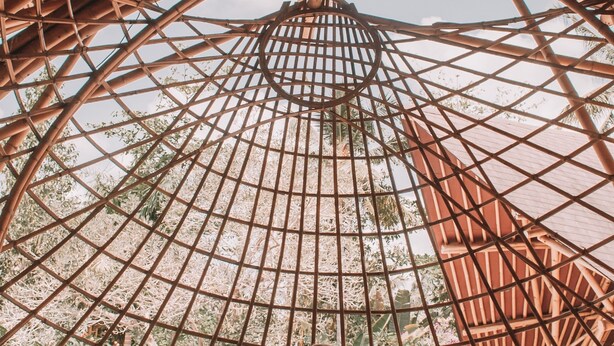 A person sitting on a wooden deck under a large bamboo structure with a grid-like roof, surrounded by greenery. - Royal Casa Ganesha (Mas)