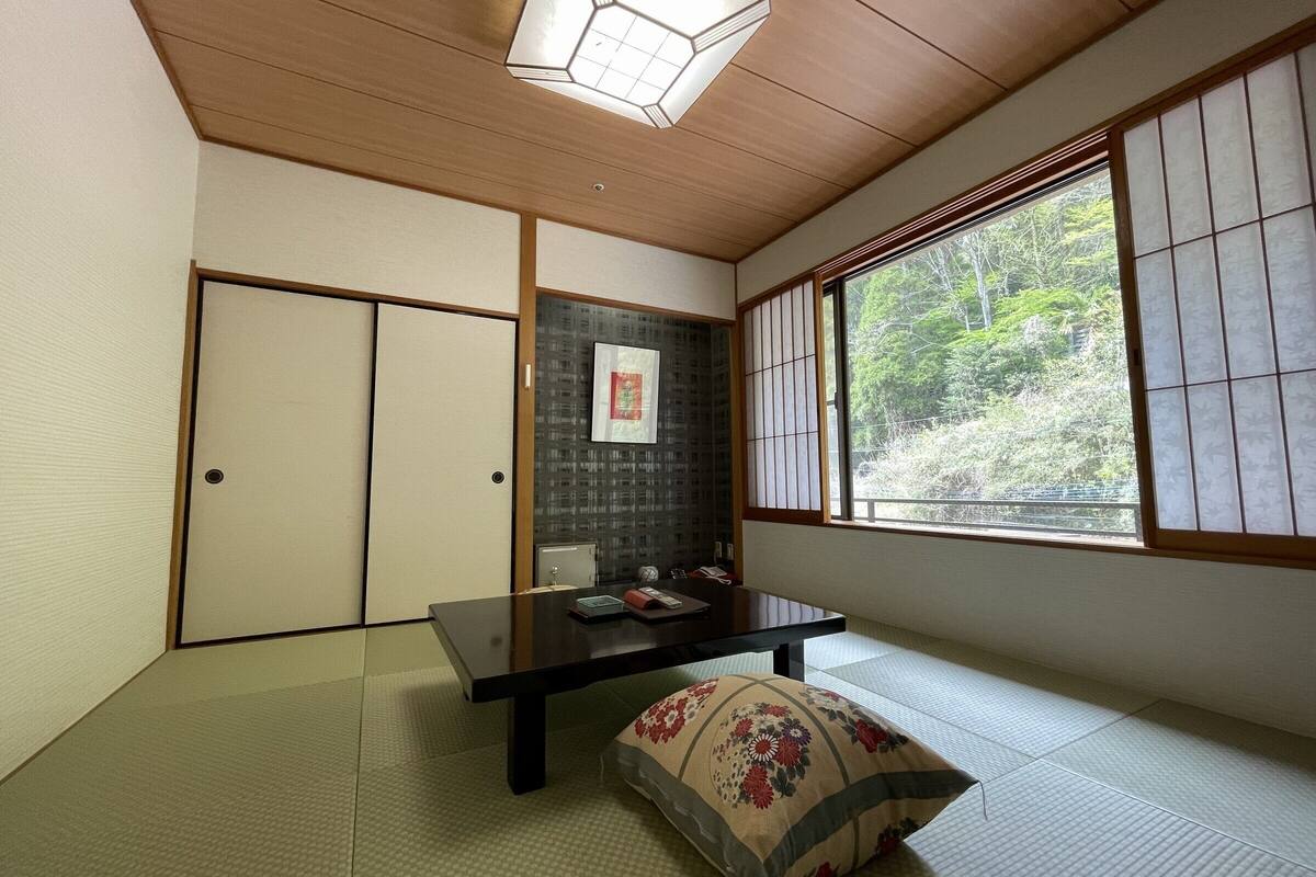 A traditional Japanese room with tatami flooring, a sliding door, a low table, and a window with shoji screens.