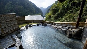 A traditional Japanese onsen with a stone bath surrounded by wooden structures and a mountainous backdrop. - Tsuetate Keiryu no Yado Daishizen (Oguni)