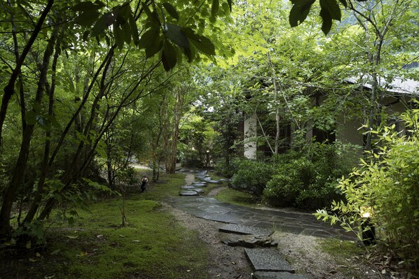 Un sendero de piedra que atraviesa un jardín exuberante, con follaje denso y un edificio tradicional al fondo.
