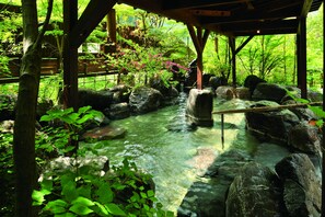 Un jardín japonés tradicional con un arroyo cristalino, rocas grandes y abundante vegetación.