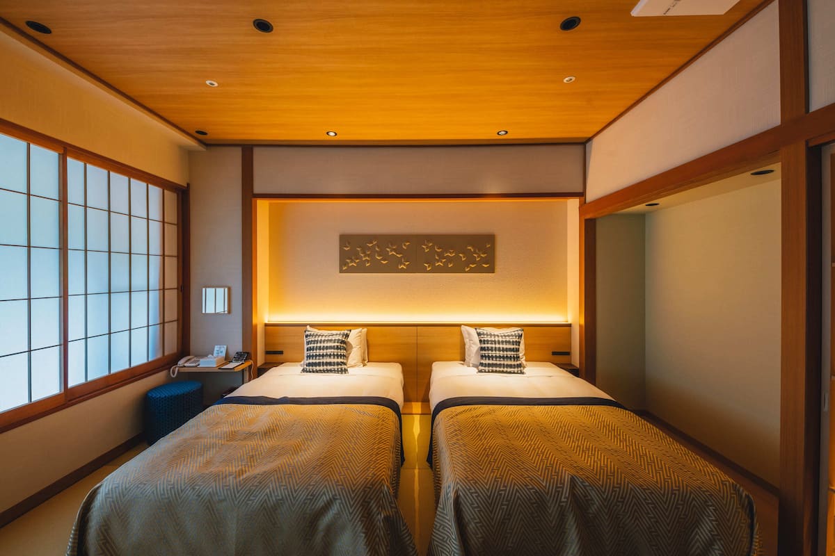 A hotel room with two beds, a wooden ceiling, and a large window with a view.