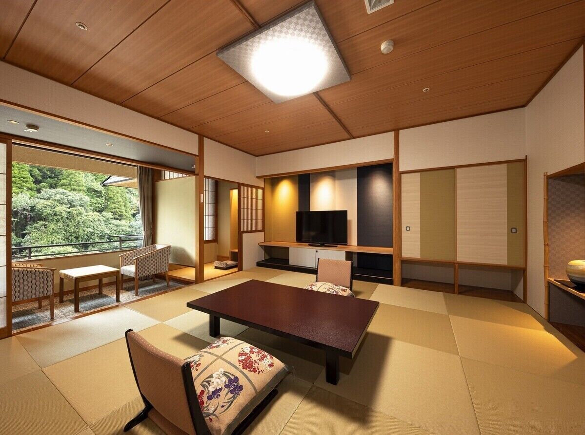 A traditional Japanese room with tatami flooring, a low table, chairs, a television, and sliding doors.