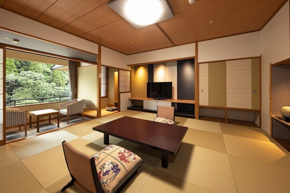 A traditional Japanese room with tatami flooring, a low table, chairs, a television, and sliding doors.