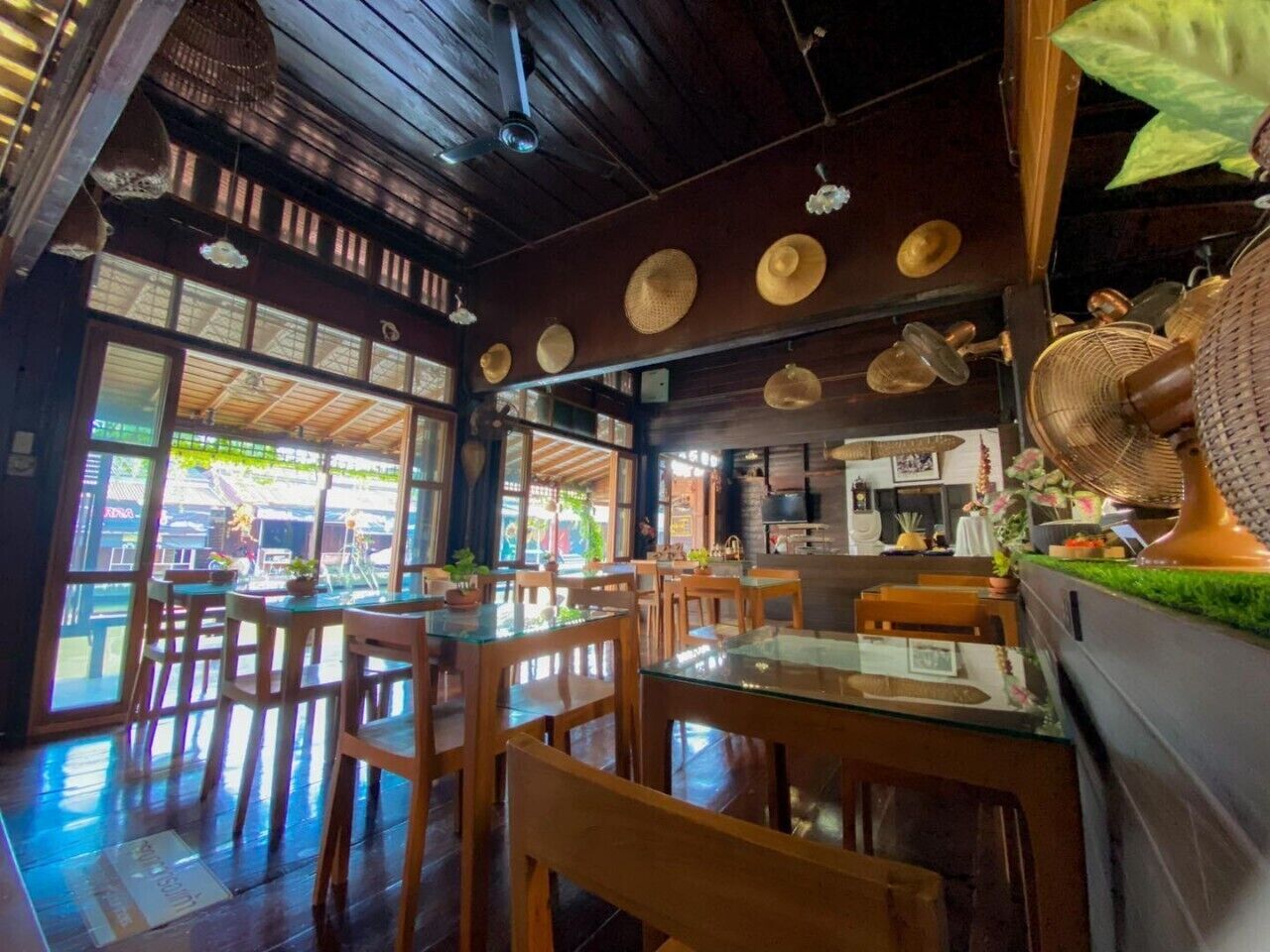 Ein Restaurant mit Holztischen, großen Fenstern und Deckenventilatoren.