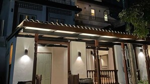 Un edificio de dos pisos con un porche cubierto, grandes macetas y un banco de madera.