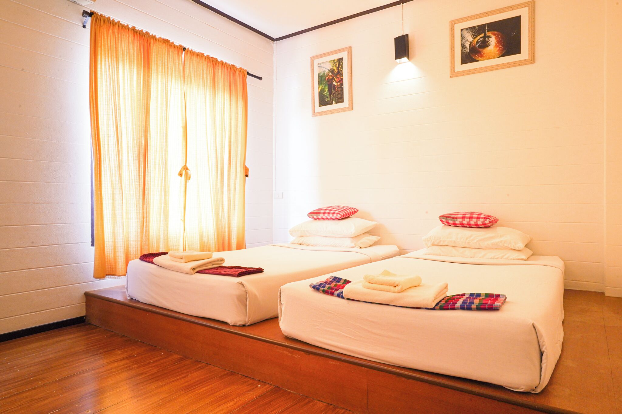 A room with two beds, a window with curtains, and two framed pictures on the wall.